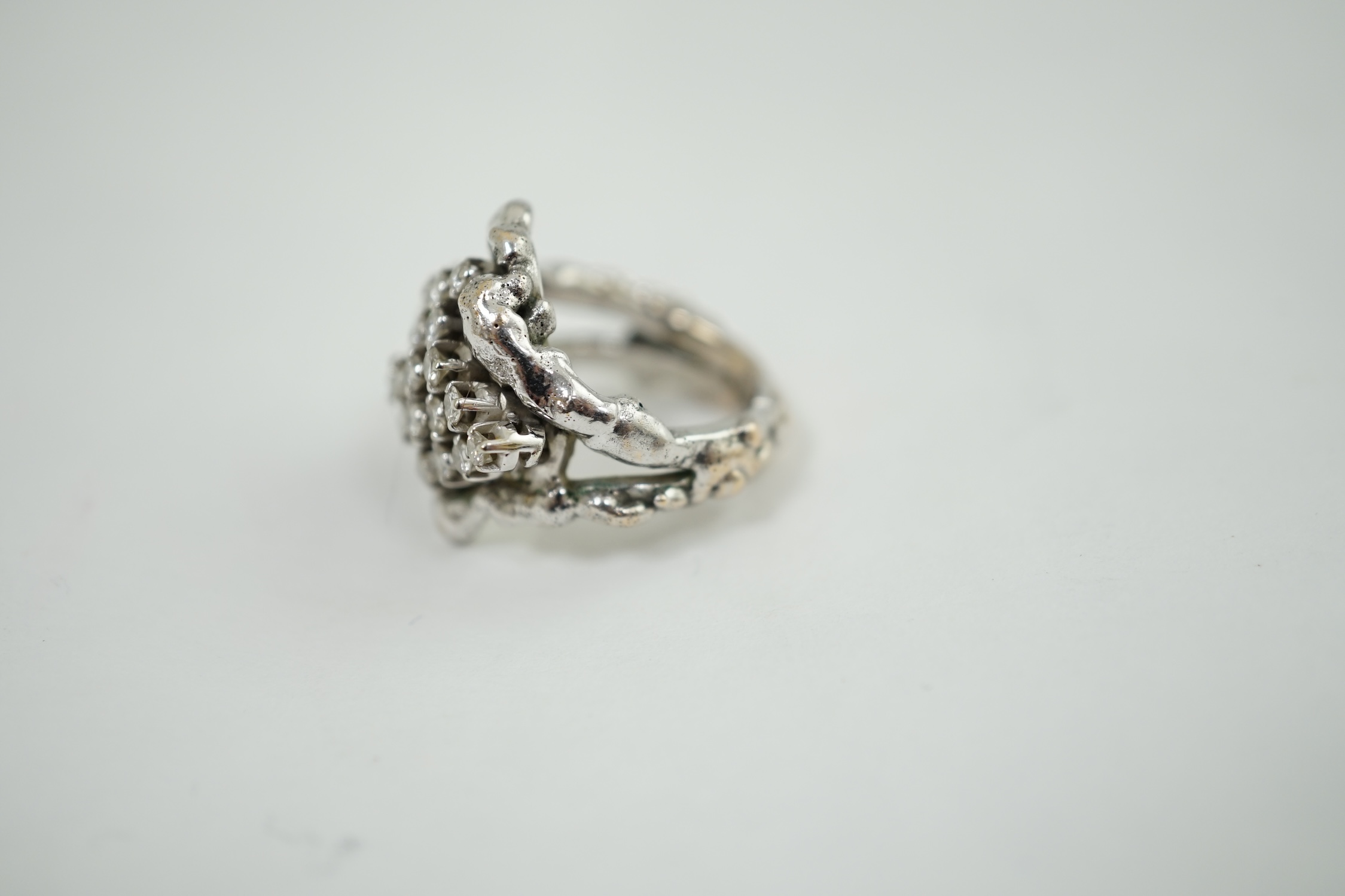 A modernist cast unmarked white metal dress ring, claw set with twenty small diamonds